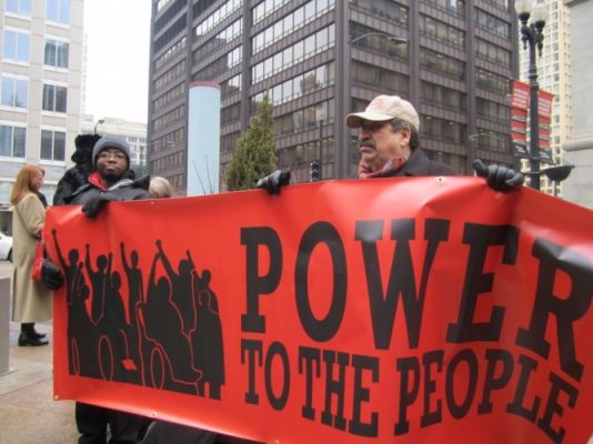 Image of people with disabilities holding a red banner that reads "power to the people"